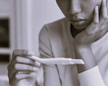 Displeased frustrated African American woman looks stressfully at pregnancy test, finds out she will become mother, looks desperately at result. Close up shot of young lady has problems with fertility